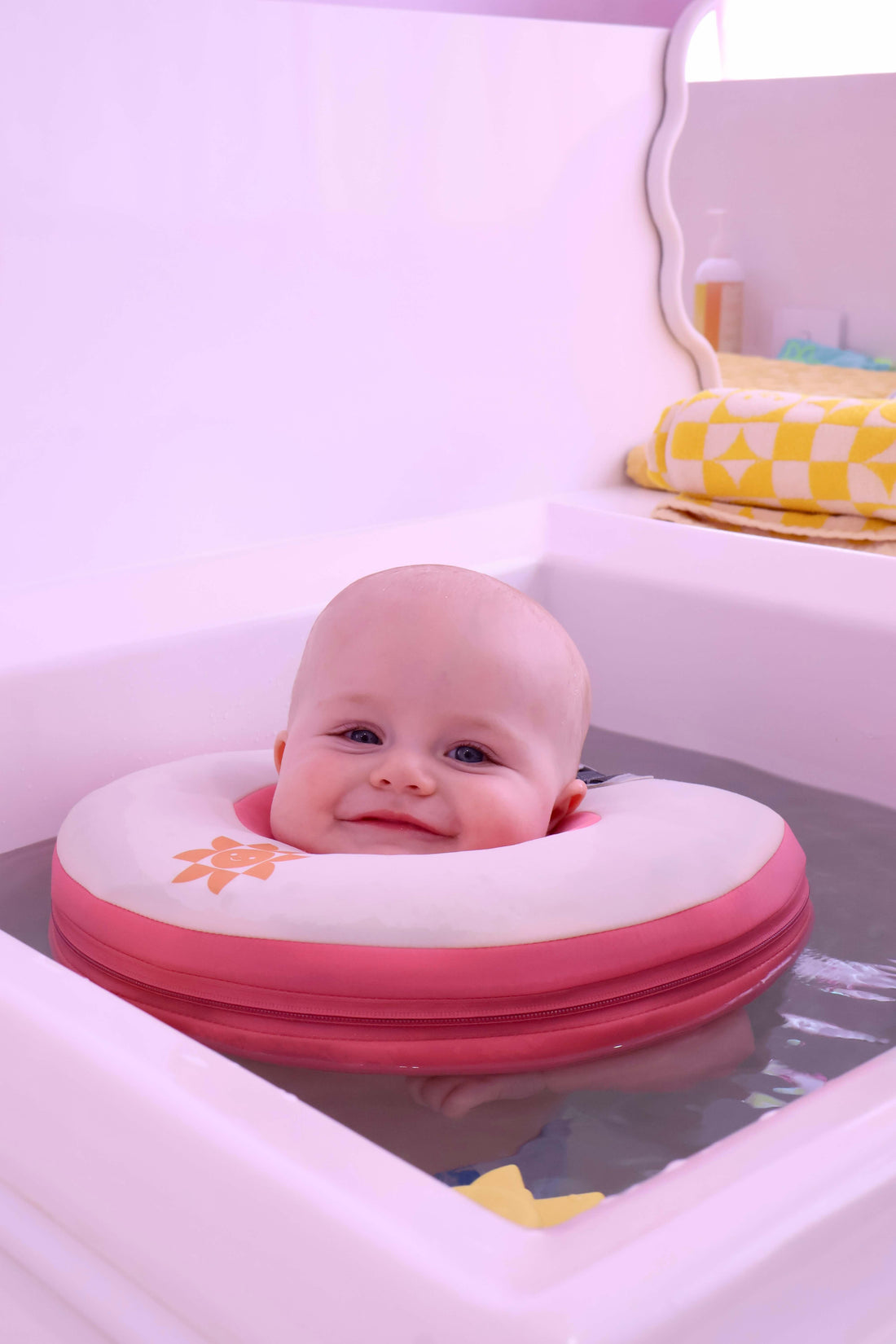 Baby in a pink inflatable bathtub seat with a white background